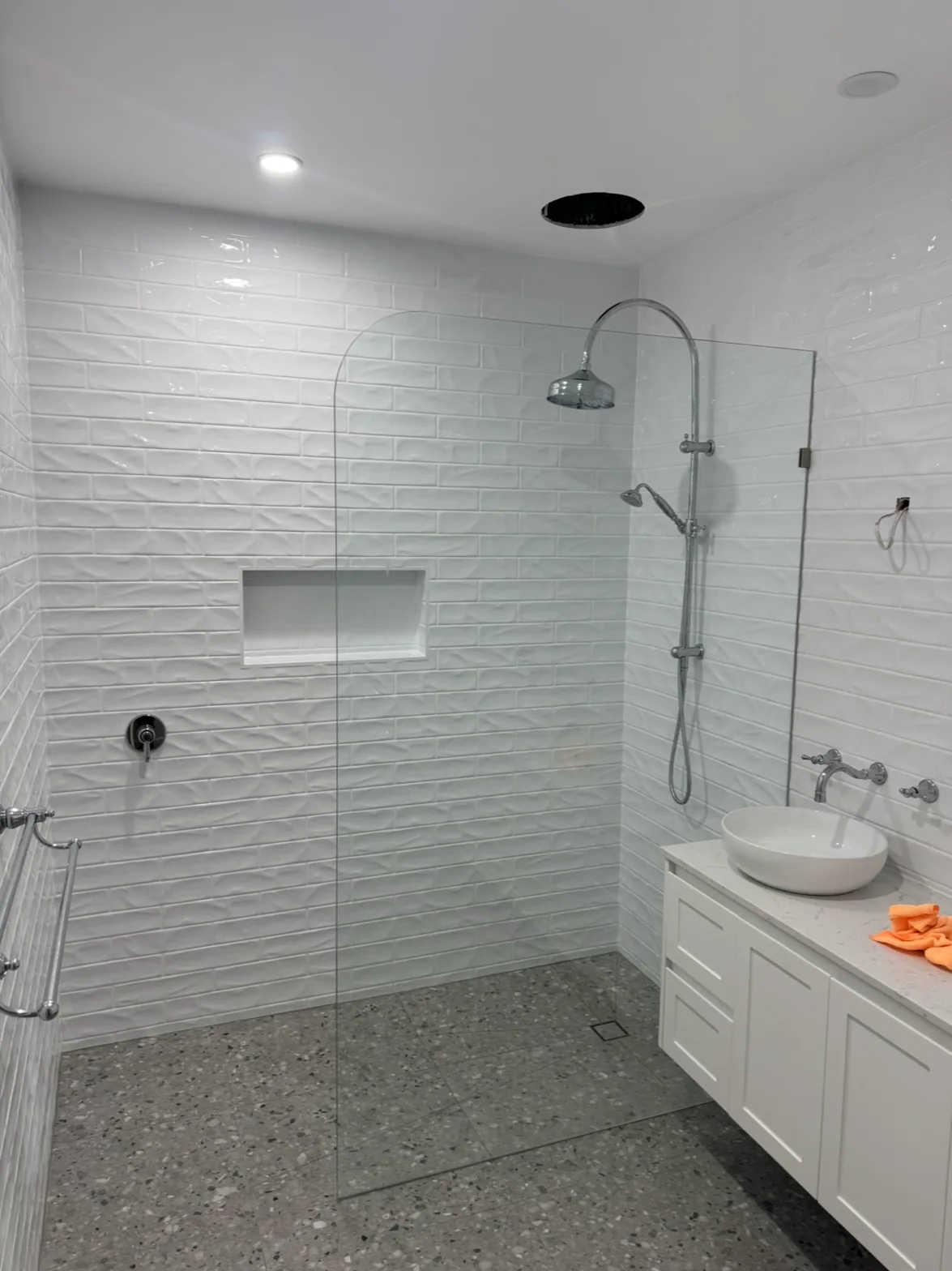 Walk-in shower with chrome rail shower set, recessed tiled niche, fixed glass panel, floating vanity with basin and wall-mounted taps